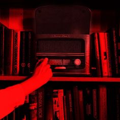 a person reaching for a radio on top of a bookshelf with red light coming from it