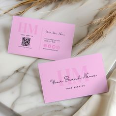 two pink business cards sitting on top of a white marble table next to dried grass