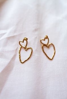 Elevate your style with our golden earrings adorned with two charming stainless steel hearts. These earrings seamlessly marry strength and romance, making them a meaningful and enduring addition to your jewelry collection. Gold Stainless Steel Anniversary Earrings, Gold Stainless Steel Earrings For Gift, Gold Stainless Steel Earrings As Gift, Heart Charm Metal Earrings For Gift, Gold Plated Double Heart Charm Earrings, Metal Heart Earrings For Wedding, Heart-shaped Metal Earrings For Wedding, Gold Hypoallergenic Heart Earrings, Yellow Gold Metal Earrings For Valentine's Day