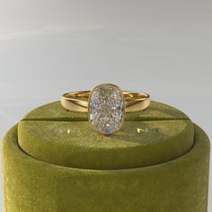 an oval shaped diamond ring sitting on top of a green velvet covered display stand with a white background