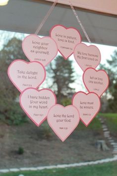 pink hearts hanging from a window with verse written on them in the shape of heart