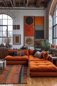 an orange couch is in the middle of a room with large windows and pictures on the wall