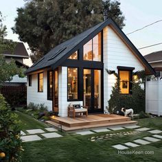 a small white house with black shingles on the front porch and steps leading up to it