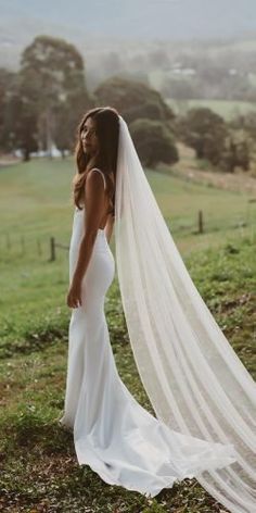 a woman in a wedding dress standing on a hill with her veil blowing in the wind