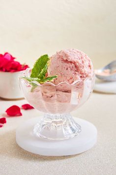 two scoops of ice cream in a glass bowl with rose petals on the side