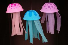 three jellyfish shaped lights hanging from strings on a black background, one is pink and the other is blue