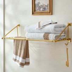 towels are stacked on a gold shelf in the corner of a room with a framed painting above it