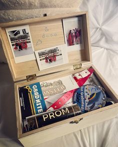 an open wooden box filled with assorted items on top of a white sheet covered bed