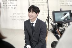 a man in a suit and tie sitting on a chair with a camera behind him