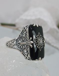 Black Glass/Stone & CZ Ring Grace Design#233 Custom Made I now offer this lovely Antique Art Deco/Edwardian design ring in sterling silver. This gorgeous ring is set with a stunning floral filigree embellished black glass/resin with a centered set 1mm white CZ. The Black glass is 18mm Long by 19mm Wide. The ring sits 19mm NS in the finger and 10mm EW on the finger. The inside of the band is marked 925 for sterling. Notice the beautiful leaf geometric design of the filigree band and setting. Elegant Gemstones With Diamond Accents For Anniversary, Antique Jewelry With Gemstone Accents For Formal Occasions, Classic Formal Jewelry With Stone Setting, Vintage Cubic Zirconia Gemstone Jewelry, Elegant Rectangular Gemstones For Formal Events, Elegant Rectangular Gemstones For Formal Occasions, Art Deco Jewelry Ring With Gemstone Accents, Victorian Filigree Ring With Accent Stones For Formal Occasions, Antique Jewelry With Gemstone Accents For Wedding