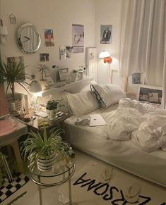 an unmade bed sitting in a bedroom next to a table with plants on it