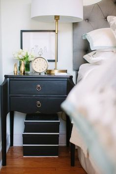 a bedroom with a bed, night stand and lamp on the side table in front of it