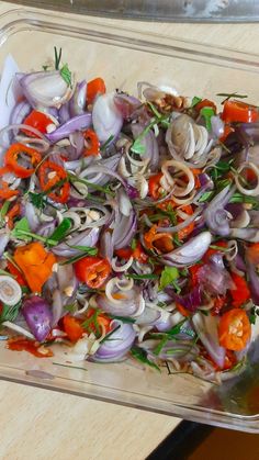 a glass dish filled with onions, carrots and other veggies on top of a wooden table