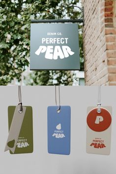 four different colored tags hanging from a brick wall next to a sign that says perfect pear