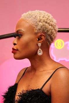 a woman with blonde hair and earrings on her head looking off to the side in front of a pink background