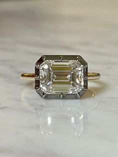 an emerald cut diamond sits on top of a marble countertop in front of a gold ring