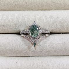 a green and white diamond ring sitting on top of two pillows