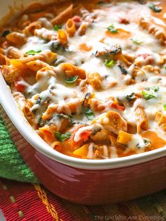 a red casserole dish filled with pasta and cheese on a colorful table cloth