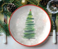 a plate with a christmas tree painted on it next to silverware and pine cones