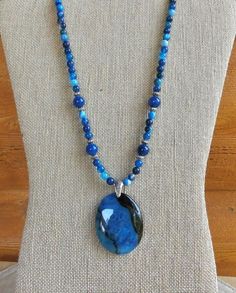 This 19 1/2 inch necklace is made from 6 mm blue striped agate beads and four 10 mm focal beads.  It also has silver accent beads and a flat silver hook and eye clasp.  The oval turquoise and black agate pendant measures about 2 inches by 1 1/2 inches.  The bail is an embossed Tibetan silver.  The blue striped agate blues have shades of turquoise from light to dark.  The matching earrings are included in the set. Blue Agate Polished Bead Necklaces, Blue Agate Beaded Necklace With Polished Beads, Blue Agate Polished Beads Necklace, Blue Agate Jewelry With Polished Beads, Blue Agate Beaded Necklaces With Natural Stones, Blue Beaded Chrysocolla Necklaces With Natural Stones, Blue Agate Beaded Necklace With Natural Stones, Blue Chrysocolla Beaded Necklaces With Natural Stones, Blue Oval Necklaces With Faceted Beads