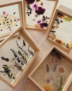 four wooden frames with pressed flowers and leaves in them on a tablecloth covered surface