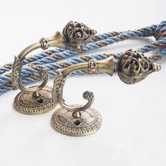 two antique style handles on a blue rope with metal fittings and knobs in the middle