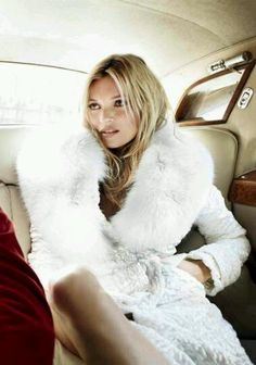 the woman is sitting in the car wearing a white fur coat and red dress with her legs crossed