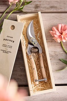 a pair of scissors sitting in a box next to some pink flowers on a wooden table