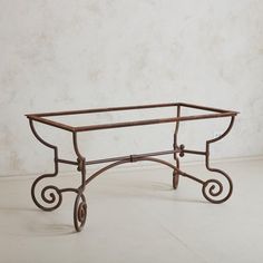 a wrought iron table with wheels on the bottom and an oval glass top, sitting against a white wall