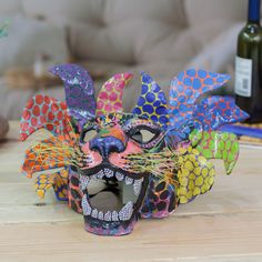 a colorful mask sitting on top of a wooden table next to a bottle of wine