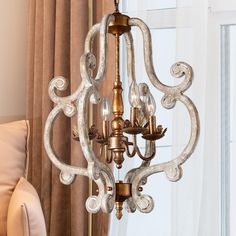 a chandelier hanging from the ceiling in a living room with curtains on the windowsill