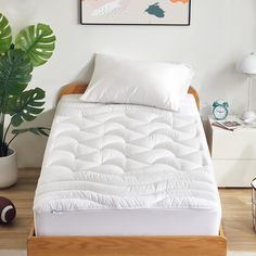 a bed with white sheets and pillows in a room next to a potted plant