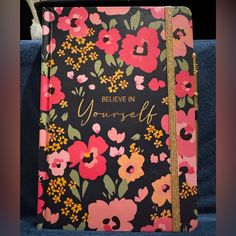 a black and pink flowered notebook with the words believe in yourself written on it