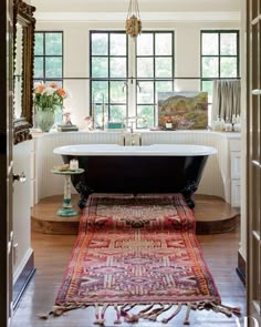 a bath tub sitting next to a wooden floor in a room with windows and rugs on the floor