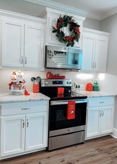 a kitchen with white cabinets and christmas wreaths on the wall above the stove top