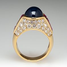 This exquisite ring is centered with an oval, sapphire cabochon in a partial bezel setting. The shoulders are each channel set with four (4) square mixed cut rubies. The top of the ring is bead set with a total of forty-six (46) round brilliant cut diamonds. The ring measures 13.7mm at the top, rises 11.2mm above the finger, tapering to 5.5mm wide and 1.3mm thick at the base of the shank. This ring is currently a size 7. Luxury Ruby And Diamond Oval Cabochon Ring, Luxury Ruby Ring With Oval Cabochon Diamond, Luxury Ruby Cabochon Diamond Ring, Luxury Oval Cabochon Ruby Ring, Luxury Cabochon Ruby Ring For Anniversary, Luxury Multi-stone Cabochons For Formal Occasions, Luxury Multi-stone Oval Cabochons, Elegant Formal Cabochon Ring, Luxury Diamond Cabochons For Formal Occasions