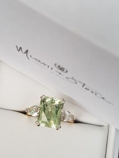 an engagement ring with a green stone surrounded by three white diamonds in a presentation box