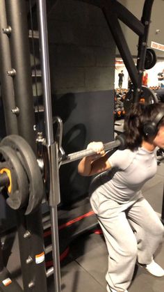 a woman is squatting in front of a gym machine with headphones on her ears