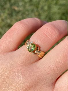 The Teleri Ladies 14K Peridot and Diamond Twist Ring. This ring is crafted in 14 karat yellow gold and centers on an oval shaped peridot stone. A delicate twist pattern in the sides of the ring lead to a small accent diamond on either side of the center. This ring is a finger size 6 and is able to be resized. Each piece has been hand selected and meticulously identified and graded by a Graduate Gemologist who has been awarded a degree by the Gemological Institute of America (GIA). Please visit o 14k Gold Green Rings With Accent Stones, Green 14k Gold Ring With Accent Stones, Green 14k Gold Rings With Accent Stones, Green 14k Gold Birthstone Ring With Accent Stones, Green Peridot Birthstone Ring For May, Green Peridot Birthstone Ring, Green Peridot Birthstone Ring For Formal Occasions, Green Peridot Birthstone Ring For Formal Events, Yellow Gold Peridot Birthstone Ring