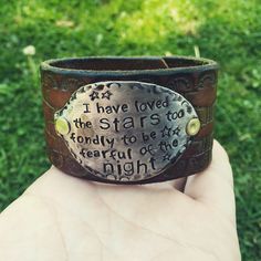 a hand holding a leather cuff with writing on it in front of some green grass