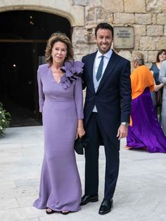 a man and woman standing next to each other in front of a stone building wearing formal attire