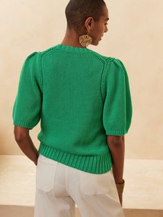 a woman in a green sweater and white pants is looking down at the back of her body