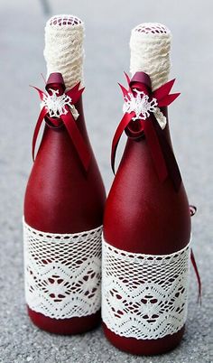 two red wine bottles with white lace and bows tied to them, sitting on the ground