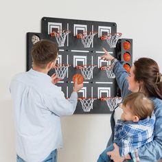 two adults and a child playing with basketballs on a wall mounted game board in the living room