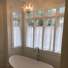 a bath tub sitting under a window next to a chandelier in a bathroom