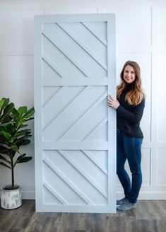 a woman standing behind a large white door in front of a potted plant on the floor