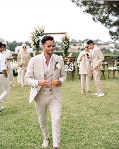 a man in a suit and tie walking through the grass with other men behind him