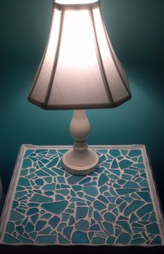 a lamp that is sitting on top of a blue table with a white base and a green wall behind it