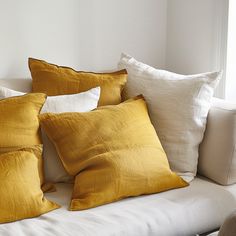 a couch with several pillows on it in front of a white wall and window sill