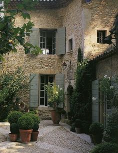 an old stone house with potted plants in the front yard and windows on each side